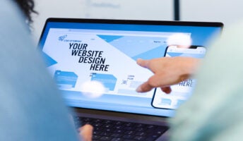 Two people gathered round a laptop with a website builder open on the screen. Source: Tech.co