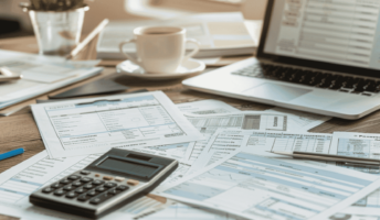 Accounting software on a laptop surrounded by papers and a calculator.